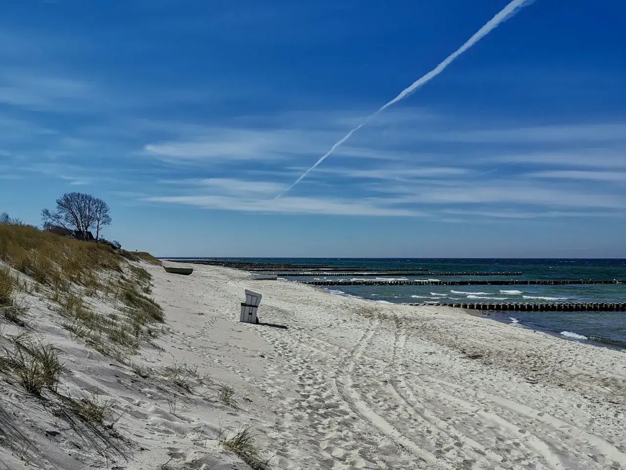 Ein einsamer Strandkorb am Ahrenshoop Strand, mit D&uuml;nen, dem Meer und einer Flugzeugspur am blauen Himmel.