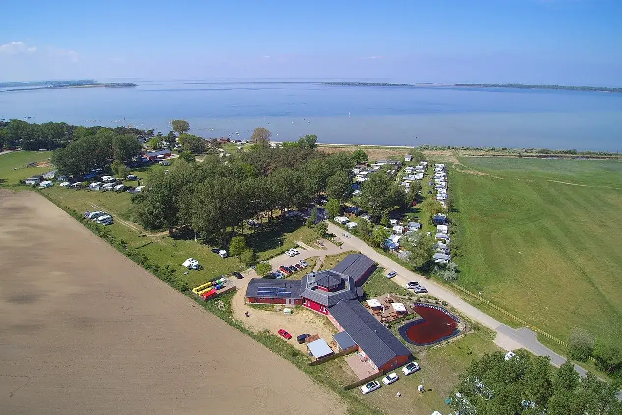 Luftaufnahme von Pepelow Camping am See mit vielen Wohnmobilen, Wohnwagen und einem roten Hauptgeb&auml;ude.