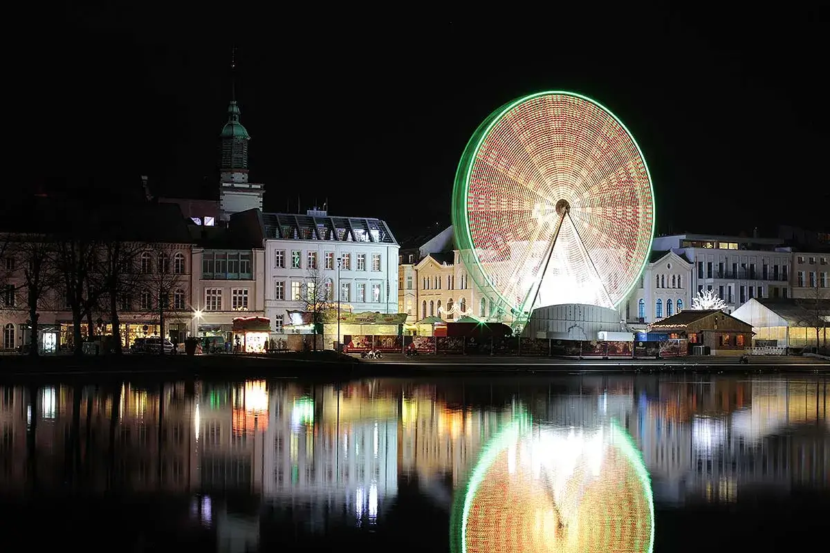 Beleuchtetes Riesenrad spiegelt sich im Wasser. Die Lichter des Altstadtfest Schwerin erhellen die Nacht.