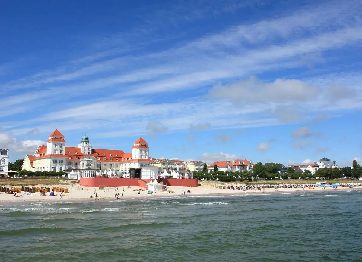 Ein sonniger Tag am Binzer Strand mit dem Kurhaus im Hintergrund. Menschen genie&szlig;en den Sand und das Meer.