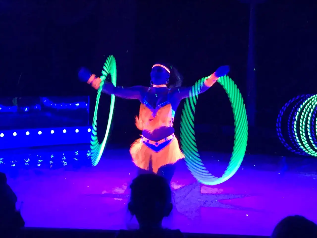 K&uuml;nstlerin wirbelt leuchtende Reifen im Dunkeln beim Circus Moreno. Neonfarben und Schwarzlicht erzeugen eine magische Atmosph&auml;re.