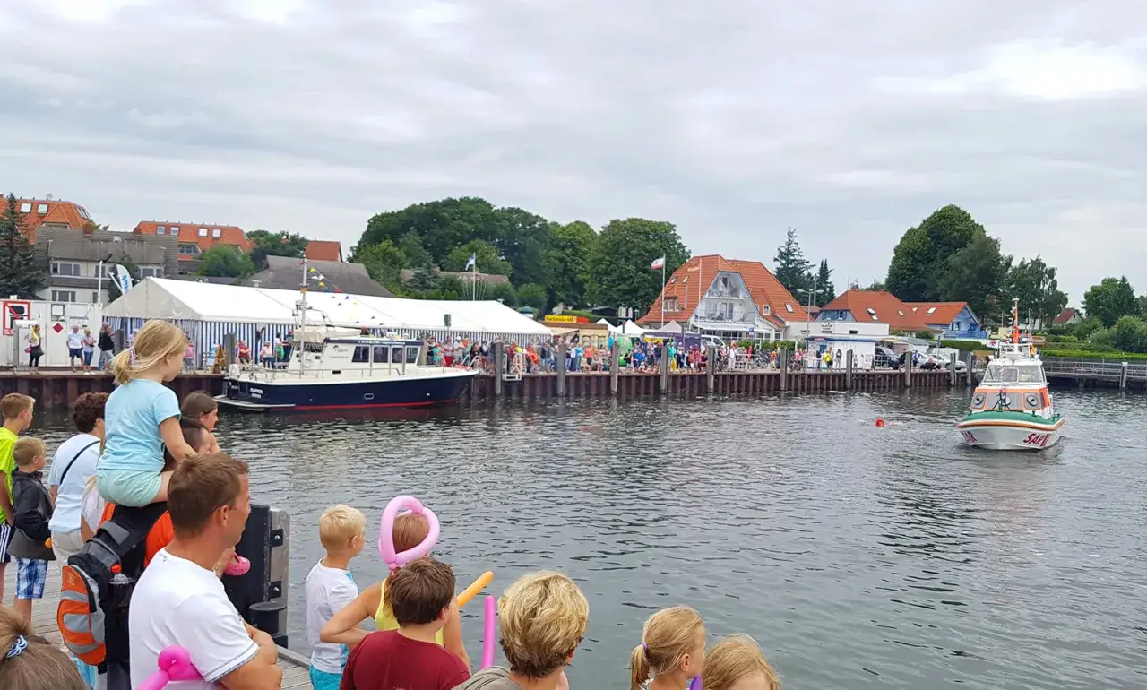Menschen genie&szlig;en das bunte Treiben beim Rock am Hafen. Boote liegen im Wasser, eine Rettungsboot f&auml;hrt vorbei.