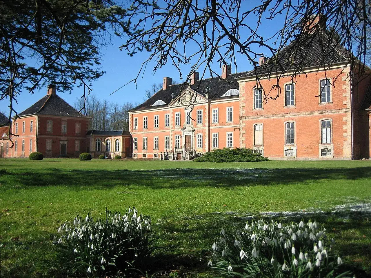 Schloss Bothmer, ein pr&auml;chtiges Backsteingeb&auml;ude, erhebt sich vor einem klaren blauen Himmel. Schneegl&ouml;ckchen bl&uuml;hen im Vordergrund.