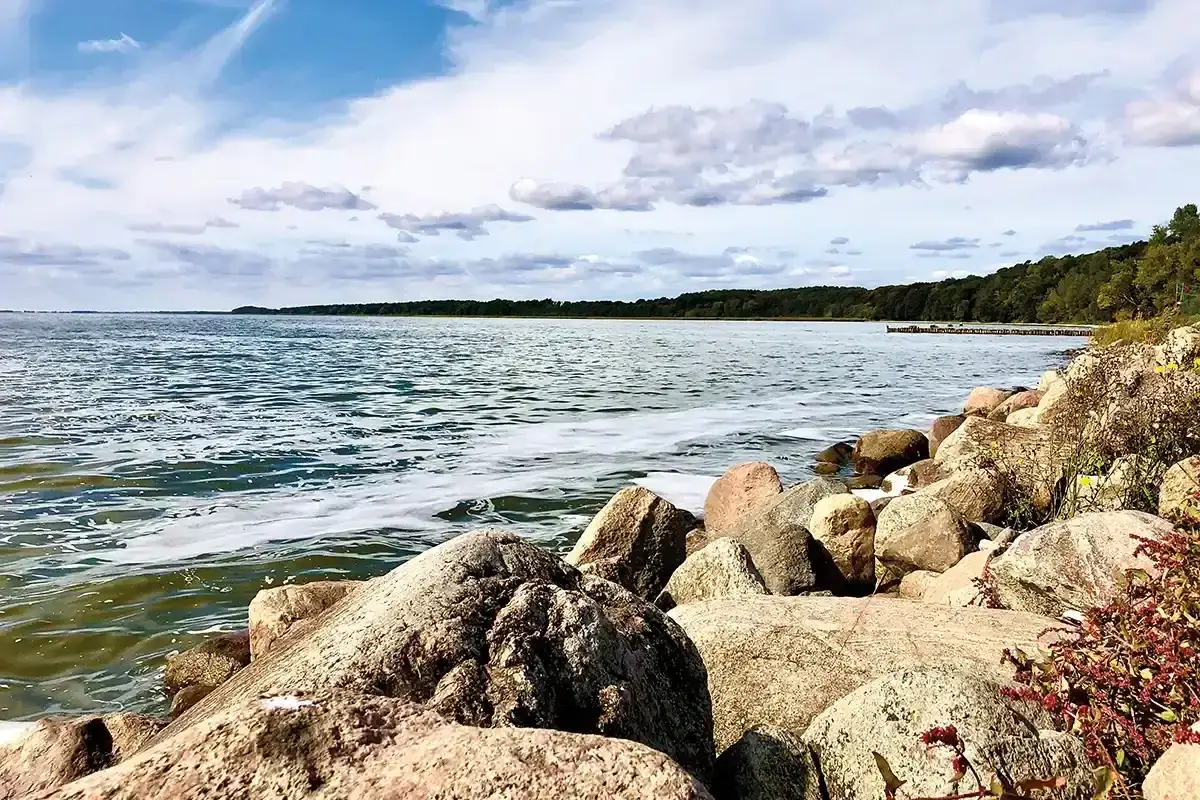 Felsen am kamminke strand. Wellen schlagen sanft gegen die Steine, im Hintergrund ein dichter Wald und ein Pier.