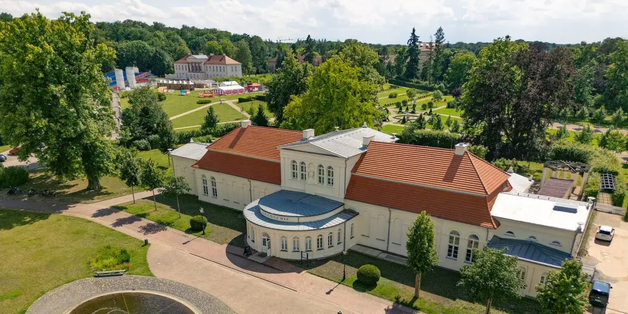 Die Orangerie Ludwigslust, ein pr&auml;chtiges Geb&auml;ude mit roten Ziegeld&auml;chern, umgeben von einem weitl&auml;ufigen Park mit B&auml;umen und gepflegten G&auml;rten.