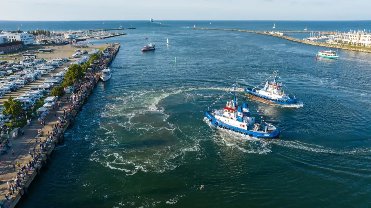 Zwei Schlepper drehen Pirouetten im Wasser, w&auml;hrend am Kai viele Menschen das maritime Festival in Rostock bestaunen.
