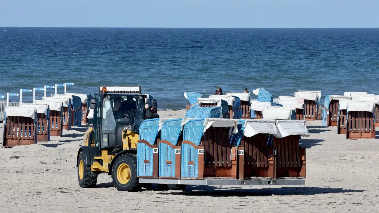 Radlader transportiert Strandk&ouml;rbe am Ostsee Strand. Die K&ouml;rbe sind blau und braun und stehen in Reihen am Sand.