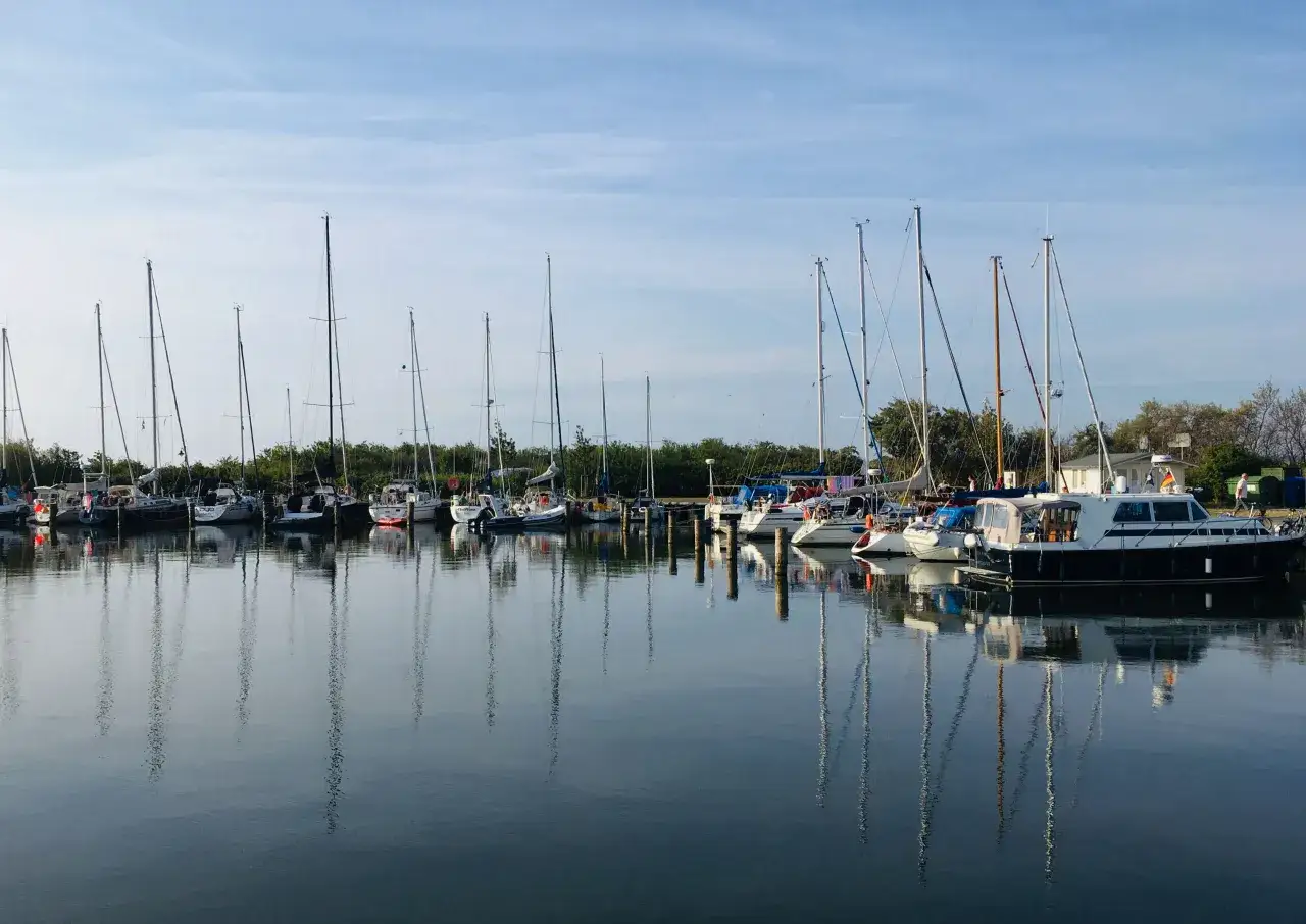 Segelboote und Yachten liegen im Hafen von Neuendorf auf Hiddensee, ihre Spiegelbilder tanzen auf dem ruhigen Wasser.