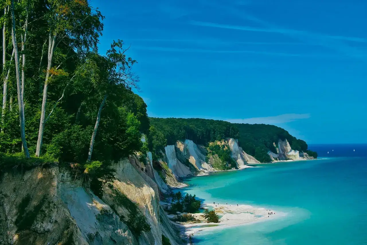 Wanderung in MV: Steilküste mit Buchenwald und Kreidefelsen, türkisfarbenes Meer, Strand mit wenigen Menschen.