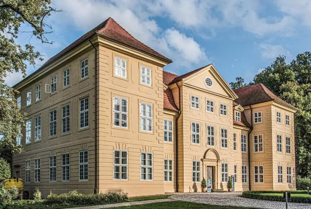 Barockes Schloss in Mirow Altstadt, umgeben von Bäumen, mit roten Ziegeldächern und vielen Fenstern.
