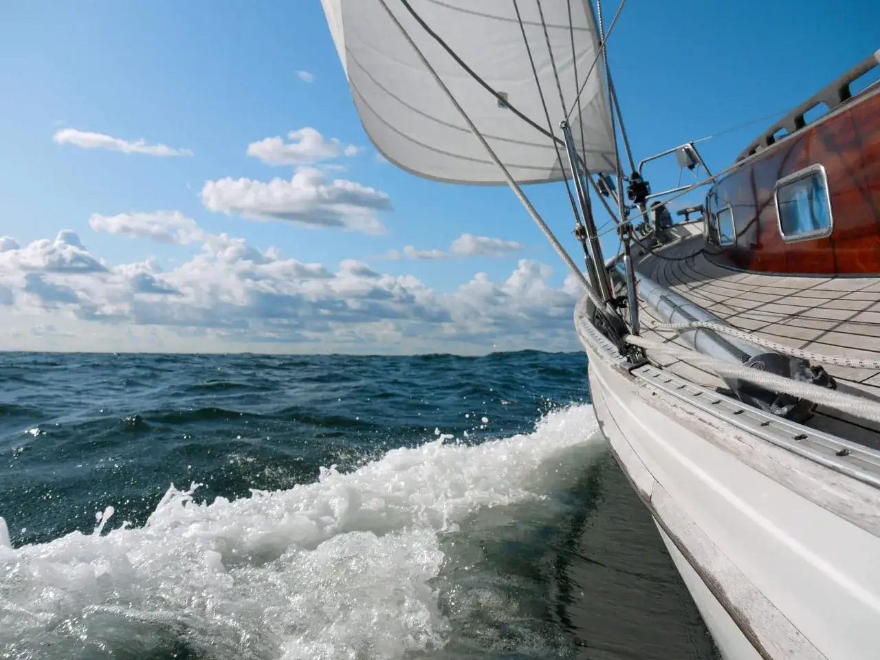 Segelboot gleitet über die Ostsee. Weiße Gischt spritzt, der Himmel ist blau mit Wolken. Ein Traum vom Ostsee segeln.