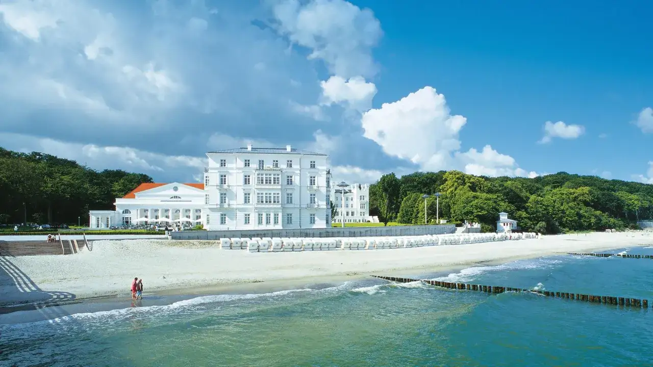 Ein wei&szlig;es Geb&auml;ude mit roten Ziegeldach am heiligendamm strand. Viele Strandk&ouml;rbe reihen sich am Sand.