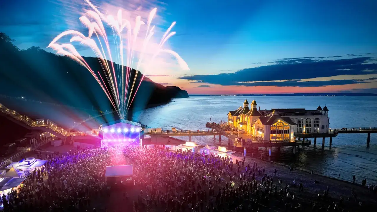 Feuerwerk &uuml;ber einem Strandkonzert an der Ostsee. Tausende feiern am Abend zu Live-Musik, w&auml;hrend bunte Raketen den Himmel erhellen.