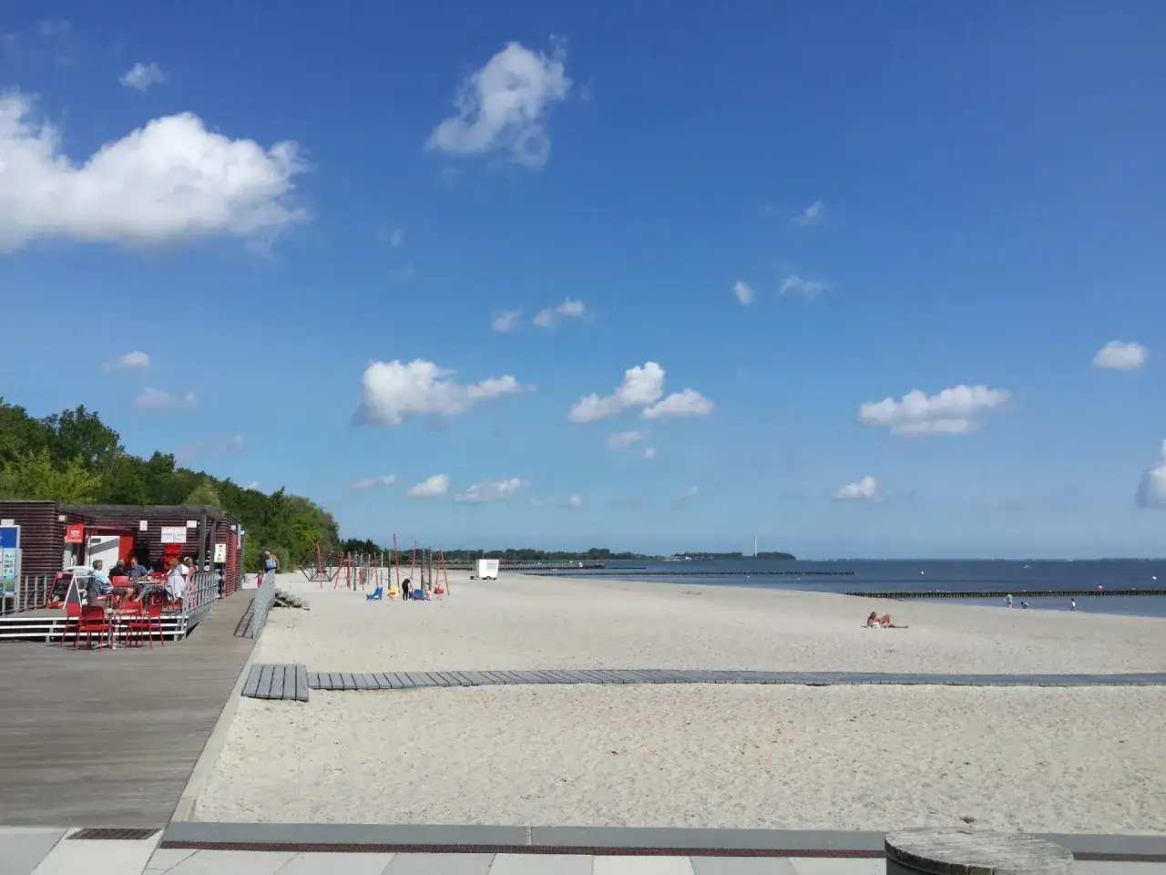 Sonniger Stralsund Strand mit Strandbar, Spielplatz und Menschen, die sich am Meer entspannen.