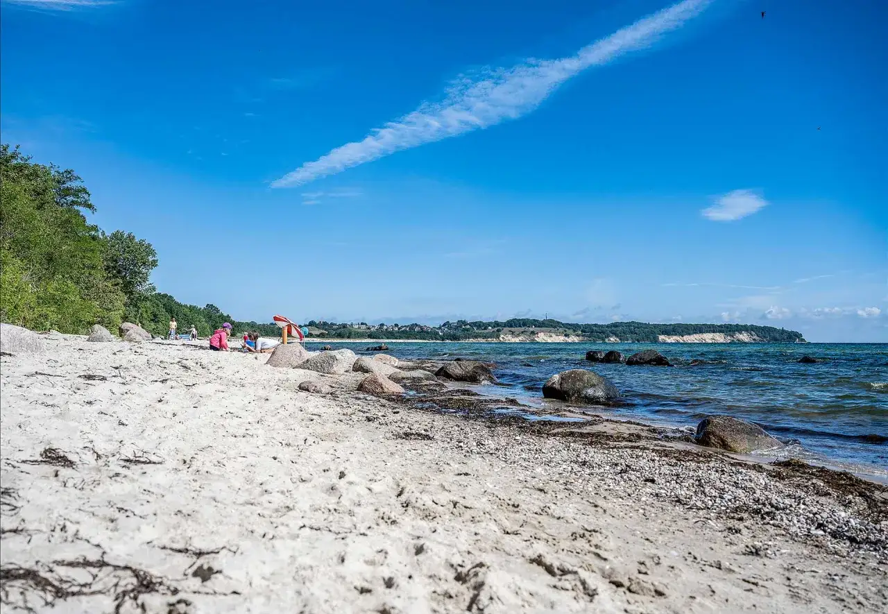 Kinder spielen am lobbe strand. Sand, Steine und das Meer prägen die Szenerie unter blauem Himmel.