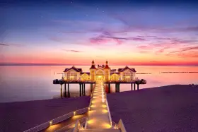 Pier mit beleuchtetem Gebäude im Abendrot, ein romantischer Blick auf die Sellin Innenstadt.