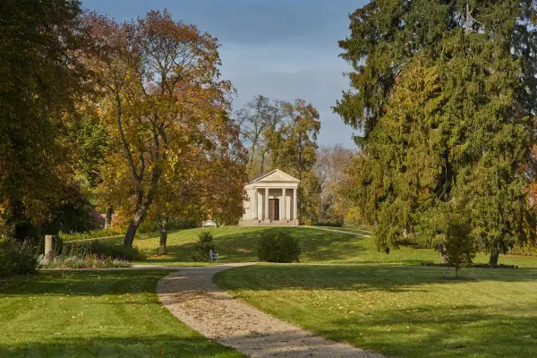 Herbstlicher Spaziergang im Schlossgarten Neustrelitz. Ein Weg führt zu einem antiken Mausoleum, umgeben von bunten Bäumen.