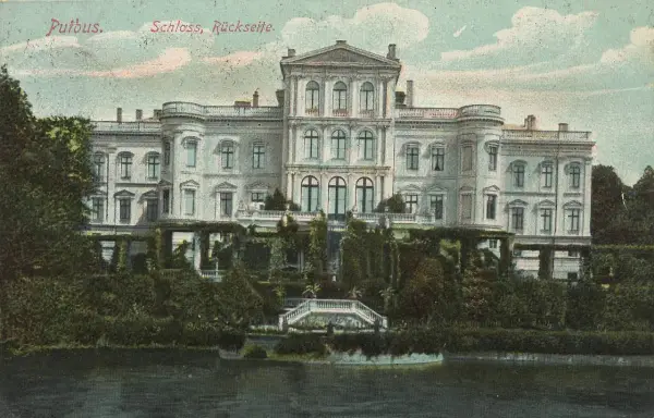 Das Schloss Putbus, von der Rückseite betrachtet, thront majestätisch über einem üppigen Garten und einem ruhigen Gewässer.