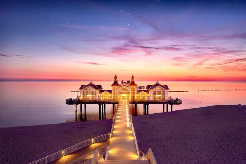 Pier mit beleuchtetem Gebäude im Abendrot, ein romantischer Blick auf die Sellin Innenstadt.