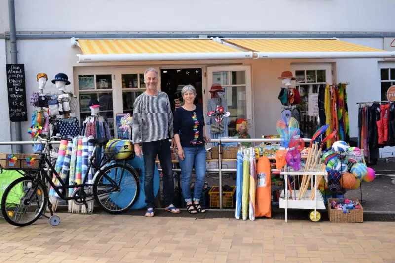 Ein Paar vor einem Laden mit Strandartikeln. Sie sind bereit, juliusruh einkaufen zu gehen und haben alles für einen schönen Tag am Meer.