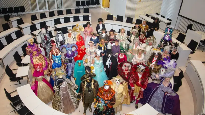 Eine Gruppe in prächtigen Kostümen und Masken, die an venezianische Tage in Schwerin erinnert, versammelt sich in einem modernen Sitzungssaal.