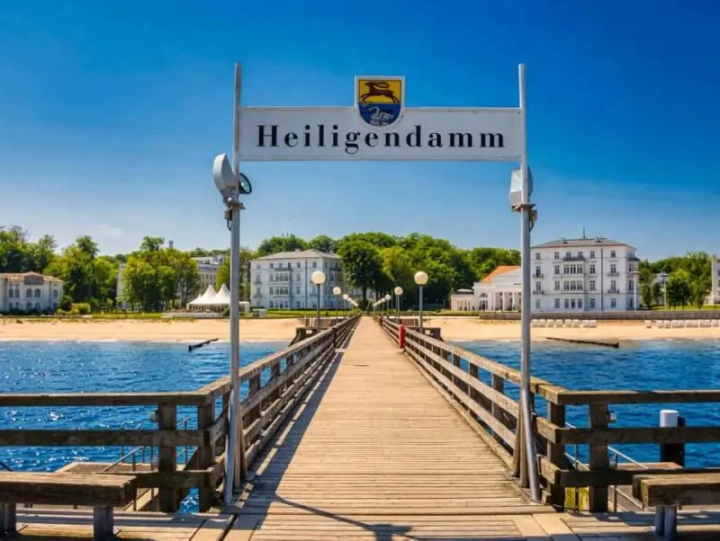 Holzsteg führt zum Heiligendamm Strand mit weißen Gebäuden und blauem Himmel.